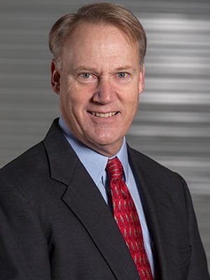 A man in suit and tie standing next to wall.